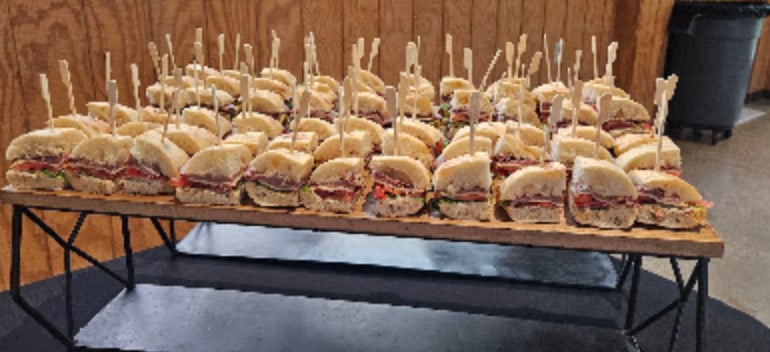 Rows of skewered deli sliders on a tiered wooden display
